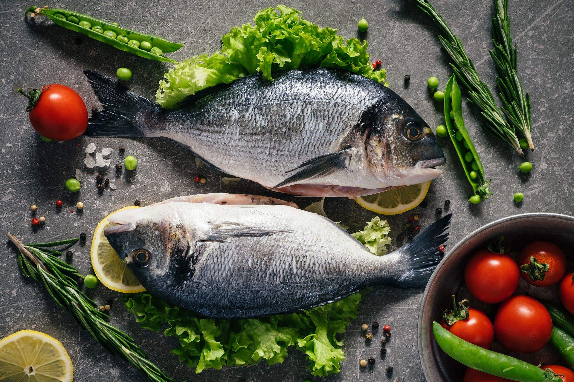 Raw dorado fish and ingredients for cooking on rustic wooden board and black background, top view