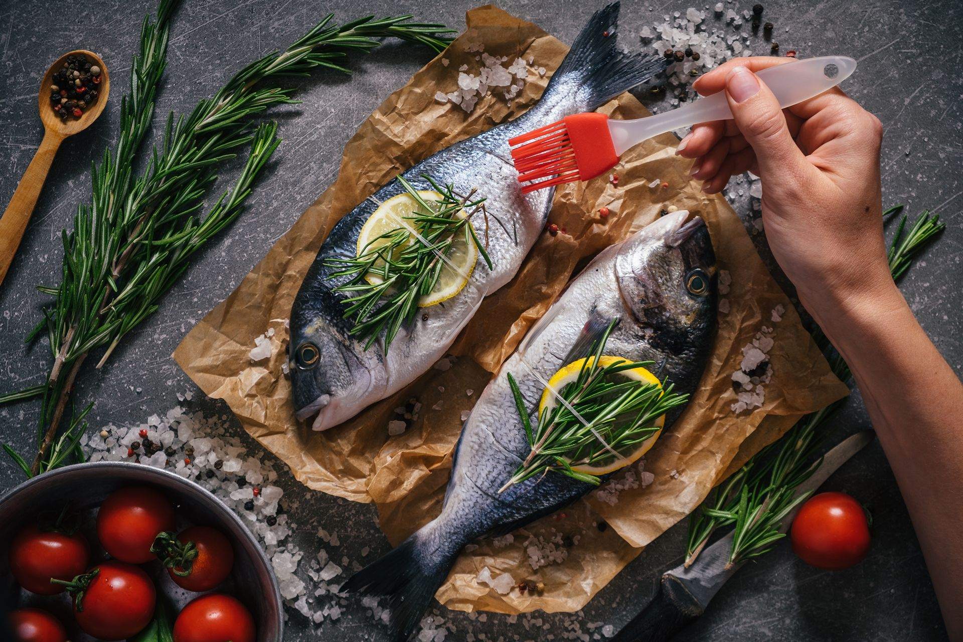 Preparing seafood fish for cooking on grill. Dorado fish with aromatic herbs and vegetables on rustic wooden board and dark background, top view