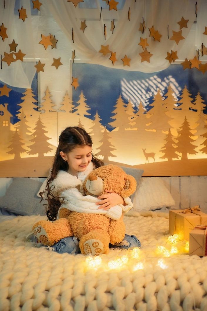 Cute little girl playing with teddy bear bed in room decorated for New Year. Winter weekends. Cozy scene. Holiday atmosphere.