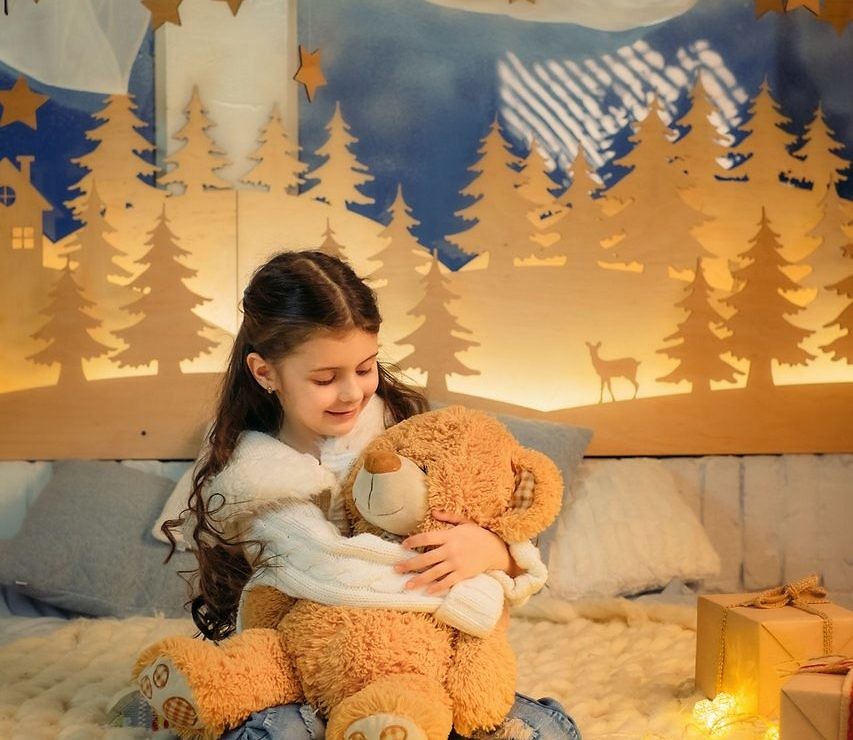 Cute little girl playing with teddy bear bed in room decorated for New Year. Winter weekends. Cozy scene. Holiday atmosphere.