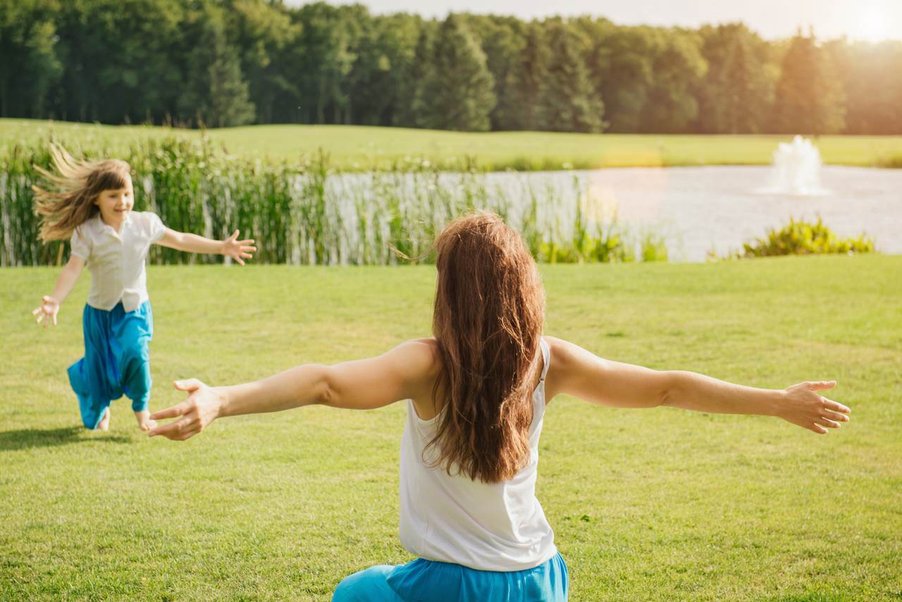 Child running into mother's hands to hug her. Family having fun in the park. Girl is happy to meet her mom