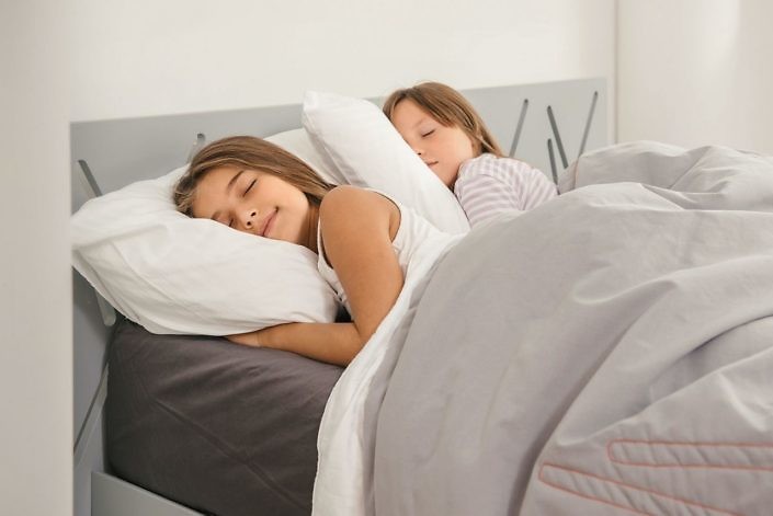 Sweet dreams of two young girls in the morning at home. Top view of bed in the room