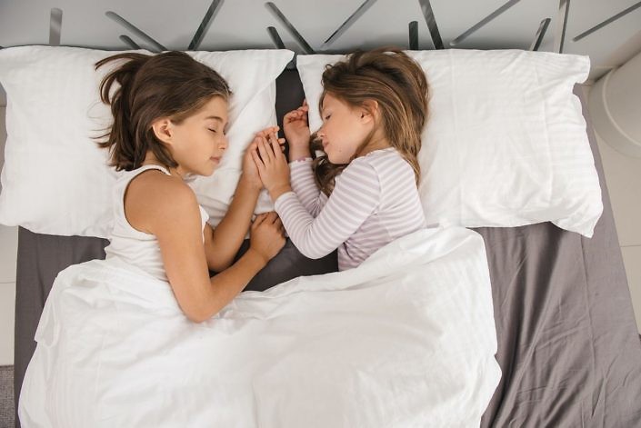Sweet dreams of two young girls in the morning at home. Top view of bed in the room
