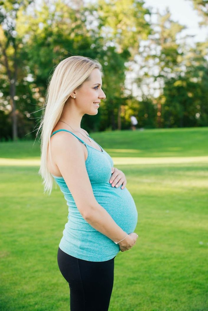 Profile view of happy pregnant women with long hair in sport costume in the park