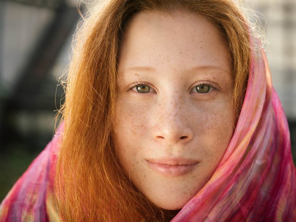Close-up portrait of red teenager girl with freckles covered with scarf outdoors