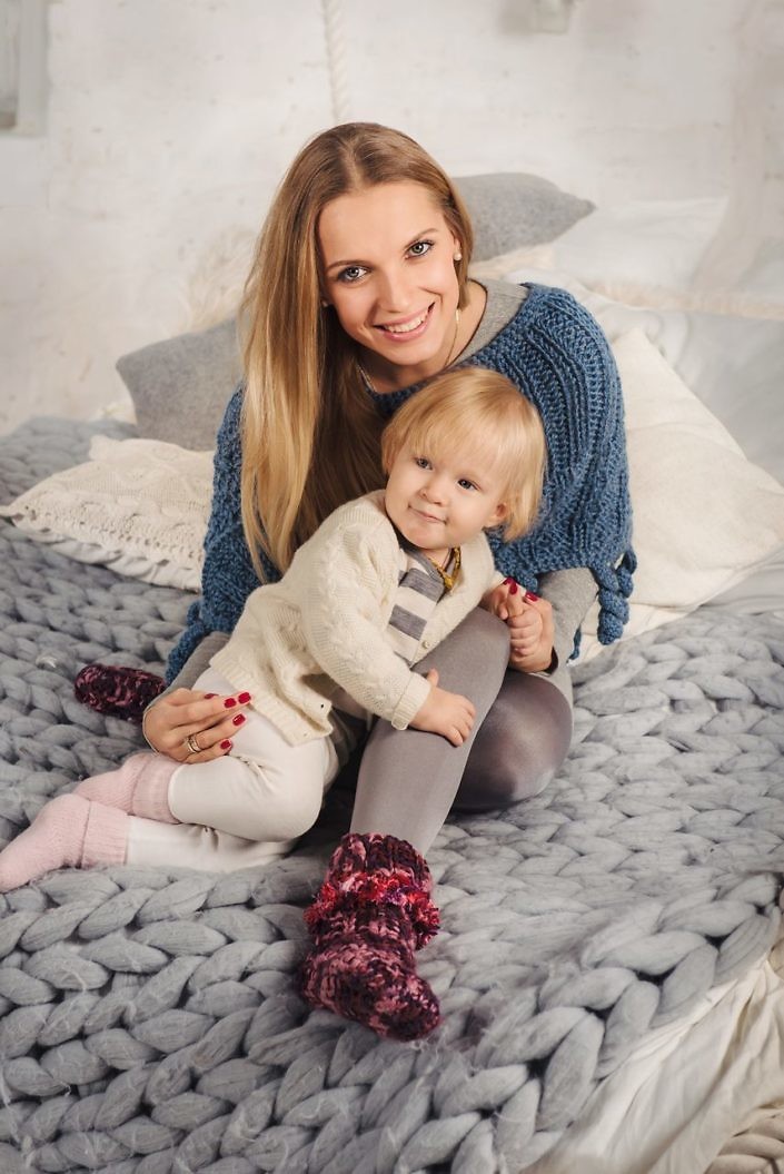 Happy blonde mother embrace her little baby daughter on the big bed in winter. Family at cozy home.