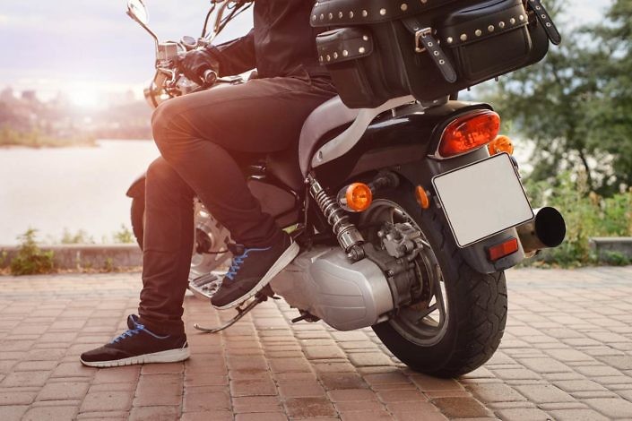 Biker having rest on motorcycle near the river in the city. Low point of view from the back